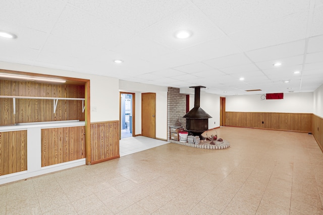 basement with a wood stove, a drop ceiling, and wooden walls