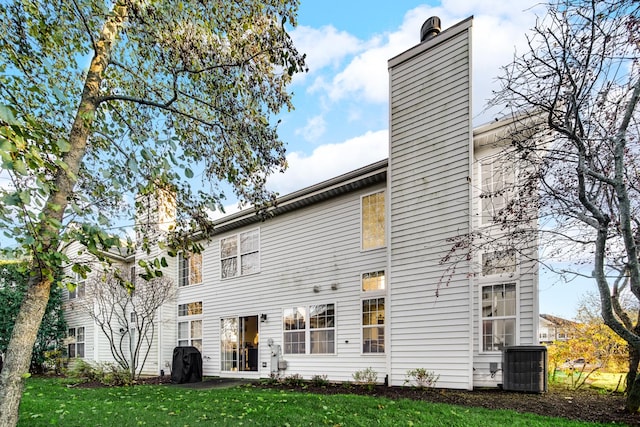 rear view of house featuring a lawn, central AC unit, and a chimney