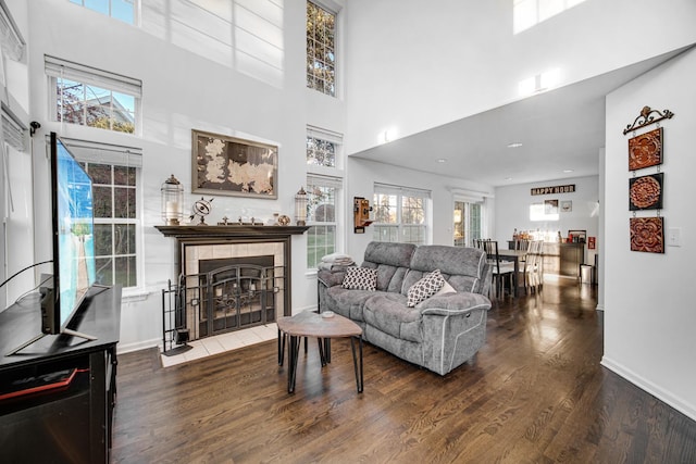 living room with a fireplace, baseboards, wood finished floors, and a towering ceiling
