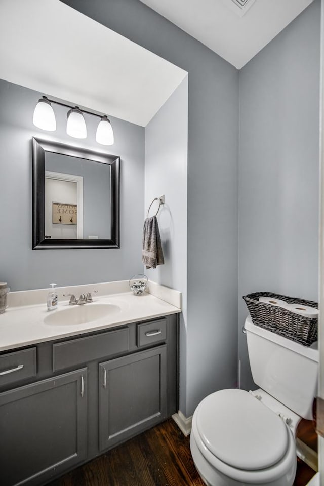 half bathroom with vanity, wood finished floors, and toilet