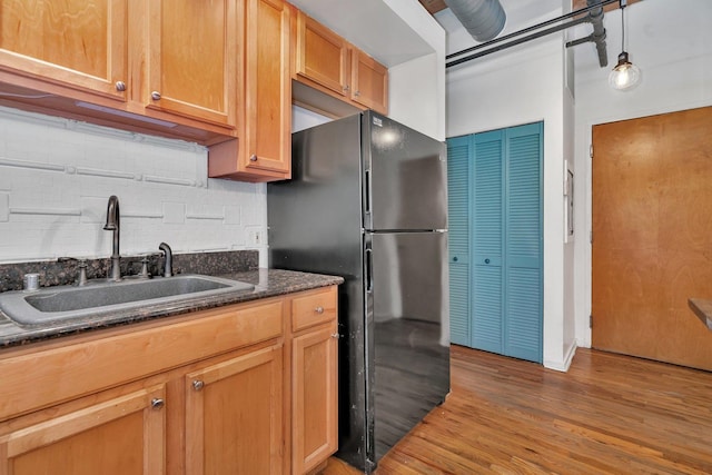 kitchen with black refrigerator, backsplash, sink, wood-type flooring, and decorative light fixtures