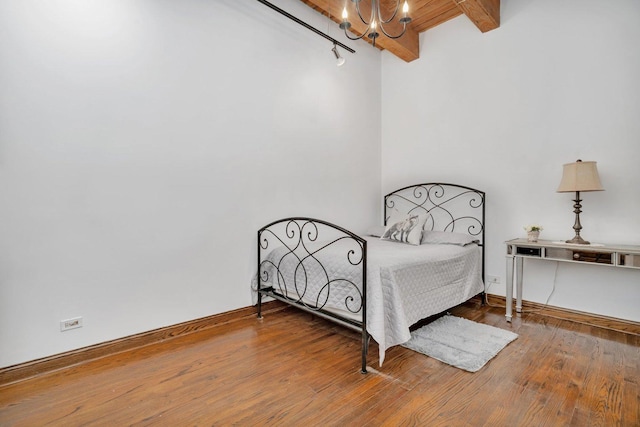 bedroom with hardwood / wood-style floors, beamed ceiling, and a notable chandelier