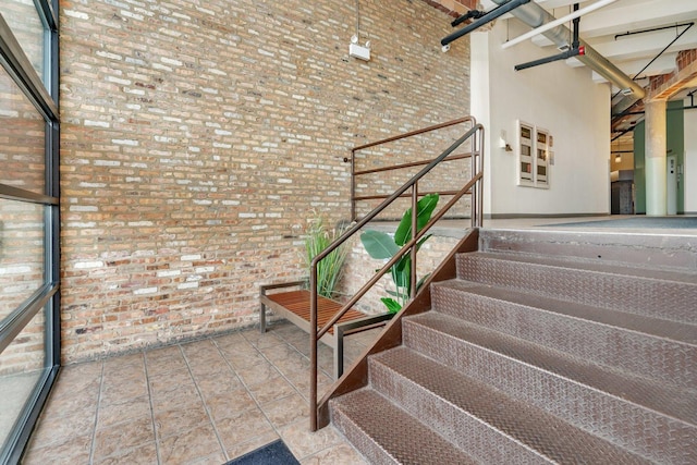 staircase featuring a towering ceiling and brick wall