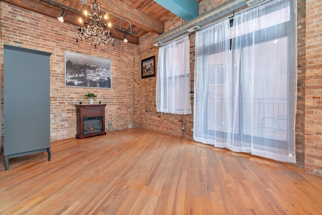 unfurnished living room featuring an inviting chandelier, beamed ceiling, brick wall, hardwood / wood-style floors, and wood ceiling