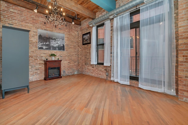 unfurnished living room featuring beamed ceiling, a notable chandelier, a fireplace, and hardwood / wood-style floors