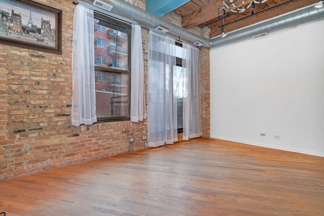 spare room featuring beamed ceiling, brick wall, and hardwood / wood-style flooring