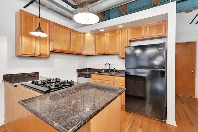 kitchen with sink, dark stone countertops, light hardwood / wood-style floors, decorative light fixtures, and black appliances