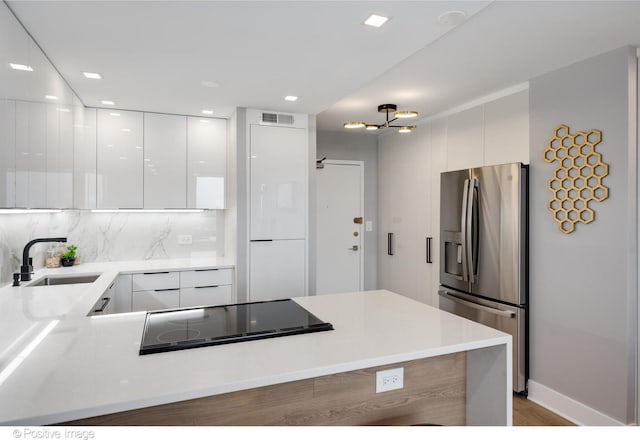 kitchen featuring black electric stovetop, backsplash, sink, stainless steel fridge with ice dispenser, and white cabinetry