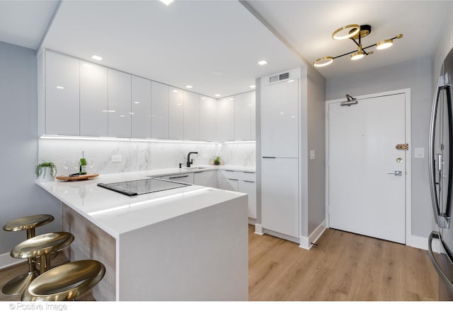 kitchen with a breakfast bar, kitchen peninsula, black electric cooktop, light hardwood / wood-style floors, and white cabinetry