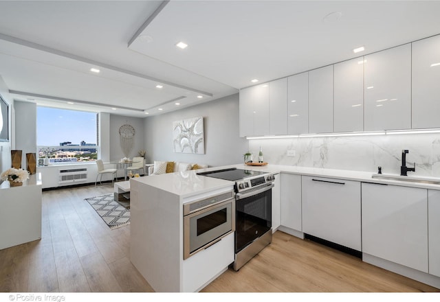 kitchen featuring kitchen peninsula, appliances with stainless steel finishes, light wood-type flooring, sink, and white cabinetry