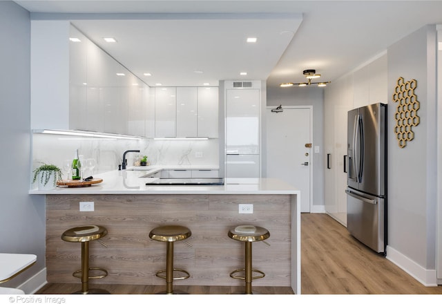 kitchen with a breakfast bar, kitchen peninsula, stainless steel refrigerator with ice dispenser, light hardwood / wood-style flooring, and white cabinetry