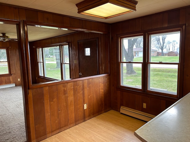 interior space featuring baseboard heating, wooden walls, and light carpet