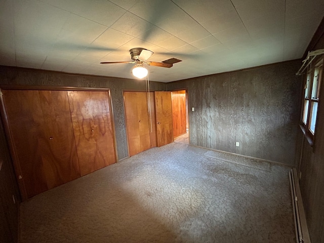 unfurnished bedroom featuring two closets, wooden walls, a baseboard radiator, and ceiling fan