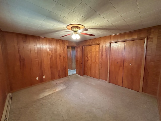 interior space featuring a baseboard radiator, light colored carpet, ceiling fan, and wooden walls