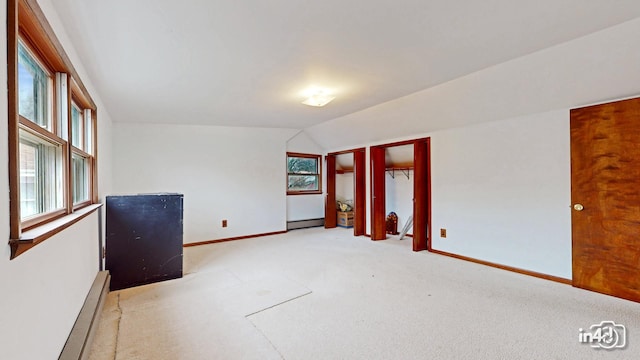 carpeted empty room featuring plenty of natural light, vaulted ceiling, and a baseboard heating unit