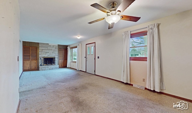 unfurnished living room with ceiling fan, a stone fireplace, and light colored carpet