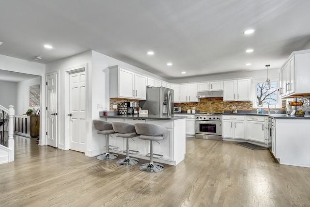 kitchen featuring a peninsula, under cabinet range hood, dark countertops, and stainless steel appliances