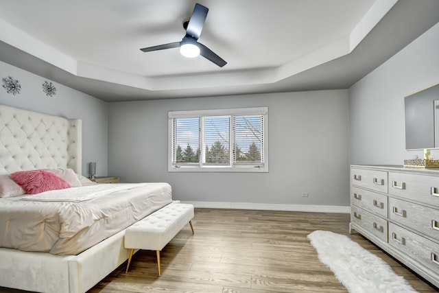 bedroom featuring a ceiling fan, baseboards, a raised ceiling, and wood finished floors