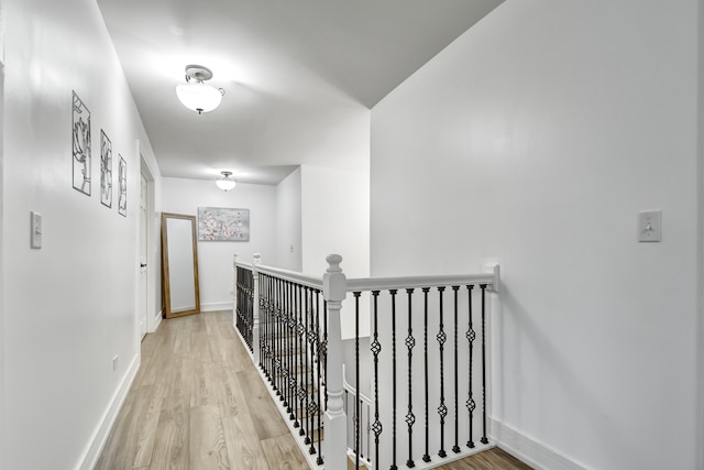 hallway with baseboards, an upstairs landing, and light wood-style floors