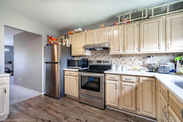 kitchen with appliances with stainless steel finishes, hardwood / wood-style flooring, tasteful backsplash, and light brown cabinetry