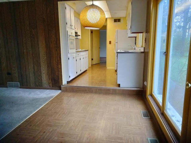 kitchen featuring white cabinetry, sink, white oven, light parquet floors, and pendant lighting