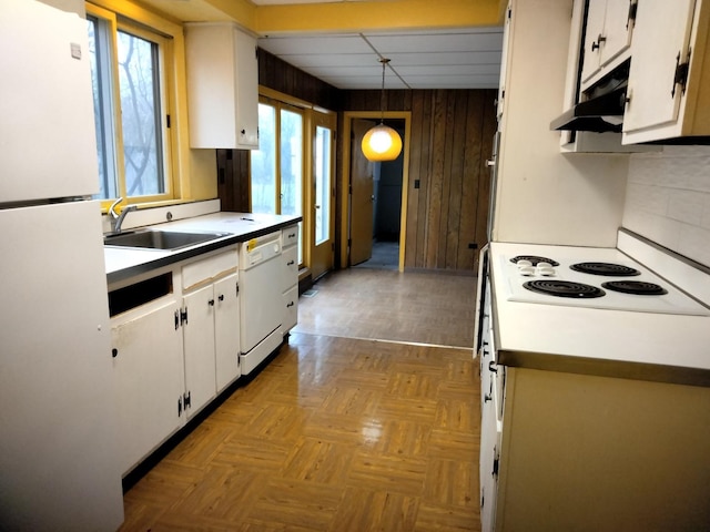 kitchen with white appliances, backsplash, wooden walls, decorative light fixtures, and white cabinetry