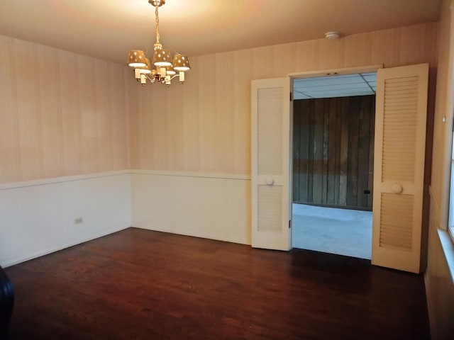 empty room with a chandelier and dark wood-type flooring