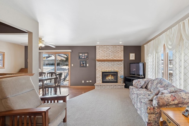 carpeted living room featuring a brick fireplace, baseboards, and ceiling fan