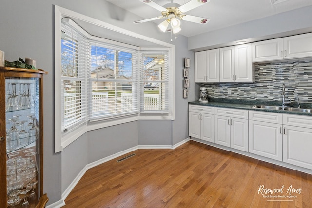 kitchen with white cabinets, decorative backsplash, light wood-type flooring, and sink