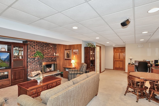 carpeted living room featuring a drop ceiling, a brick fireplace, and wood walls