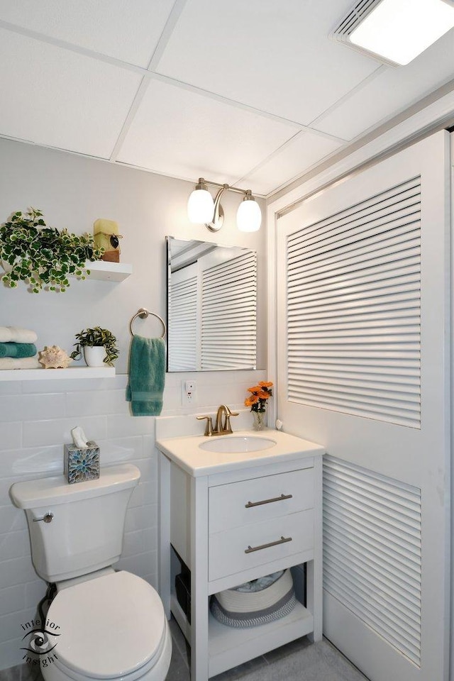 bathroom featuring vanity, a paneled ceiling, tile walls, and toilet