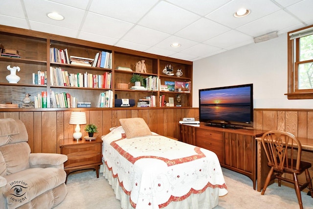 living area with a paneled ceiling, light colored carpet, wooden walls, and built in shelves