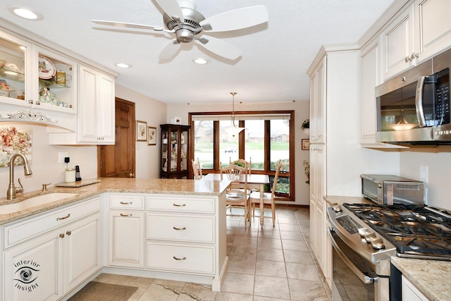 kitchen with sink, hanging light fixtures, stainless steel appliances, light stone countertops, and kitchen peninsula