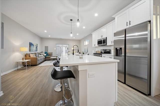 kitchen featuring white cabinets, decorative light fixtures, stainless steel appliances, and an island with sink