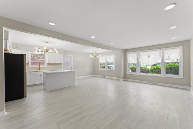 kitchen with stainless steel fridge, light hardwood / wood-style flooring, white cabinets, and decorative light fixtures