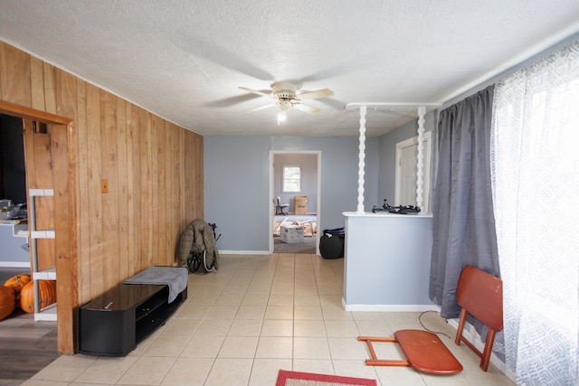 interior space with light tile patterned floors, a textured ceiling, ceiling fan, and wooden walls