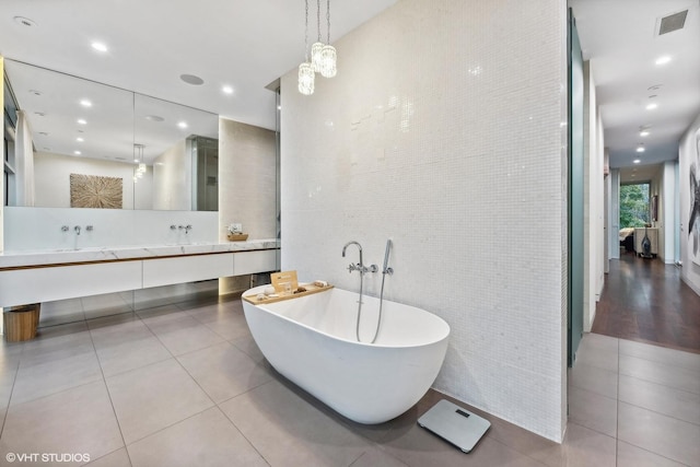 full bath featuring visible vents, tile walls, tile patterned flooring, double vanity, and a soaking tub