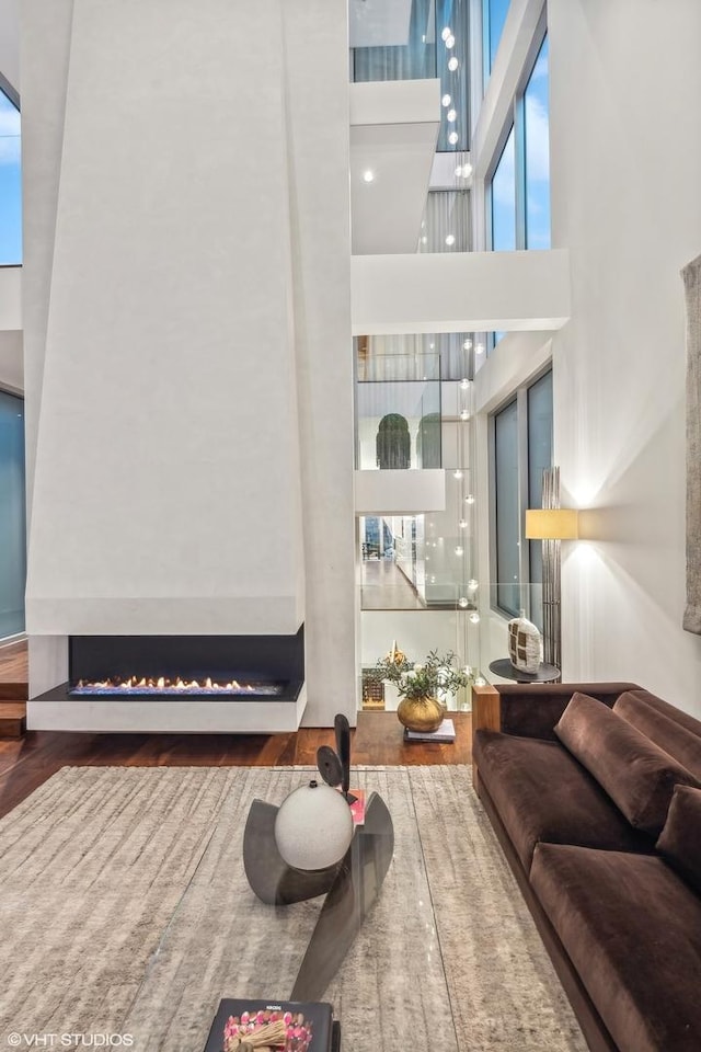 living area with a high ceiling, a lit fireplace, and wood finished floors