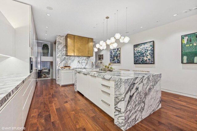 kitchen featuring a large island, light stone counters, backsplash, dark wood-style floors, and white cabinetry