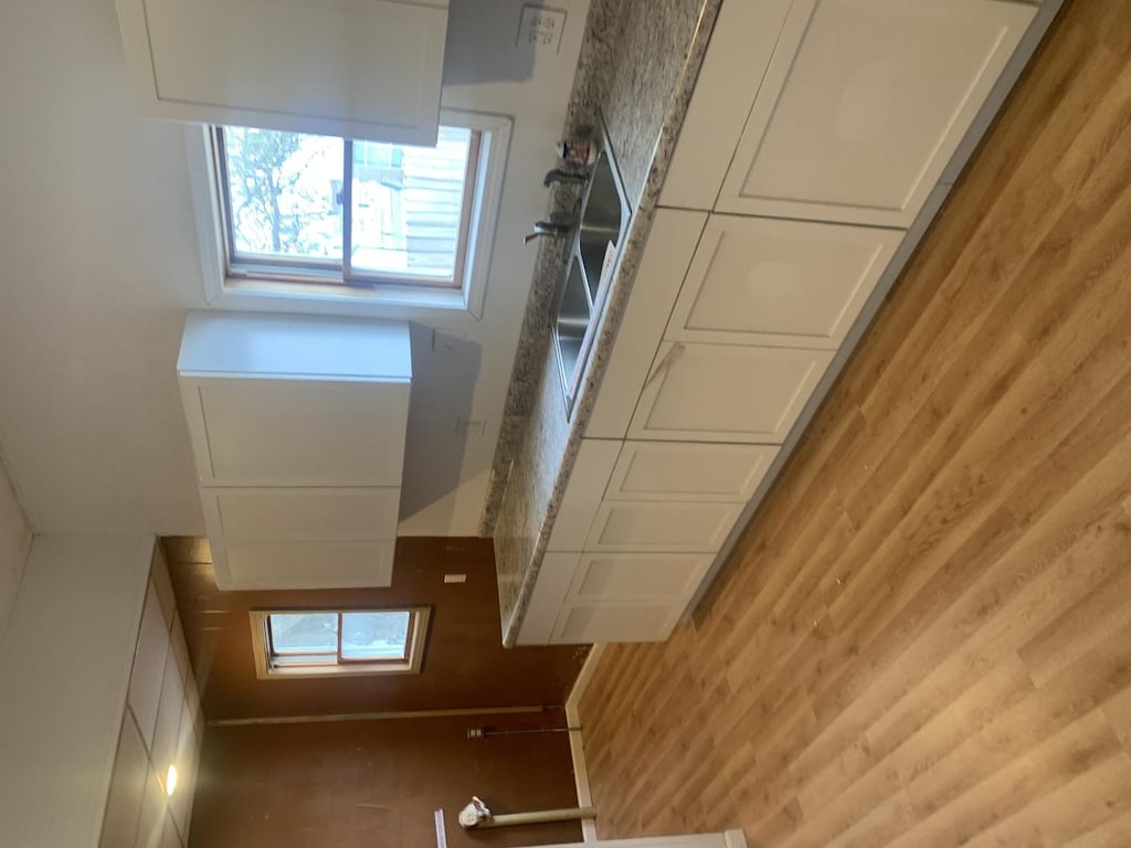 kitchen with white cabinetry, wood walls, and hardwood / wood-style flooring