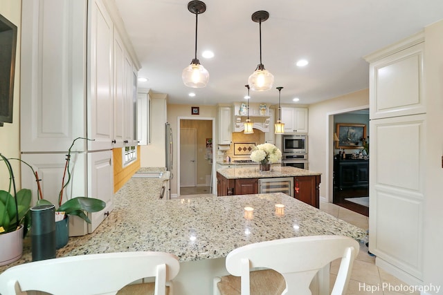 kitchen with wine cooler, light stone counters, kitchen peninsula, pendant lighting, and stainless steel appliances