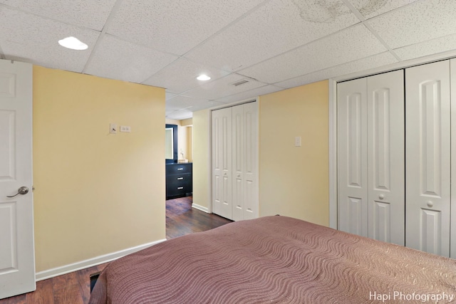 bedroom with dark wood-type flooring, a drop ceiling, and two closets