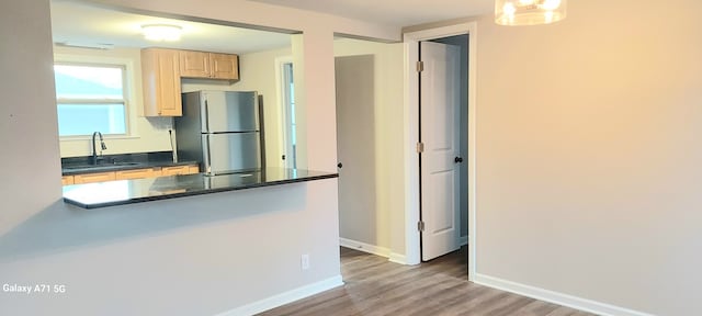 kitchen featuring stainless steel refrigerator, sink, light brown cabinetry, and hardwood / wood-style flooring