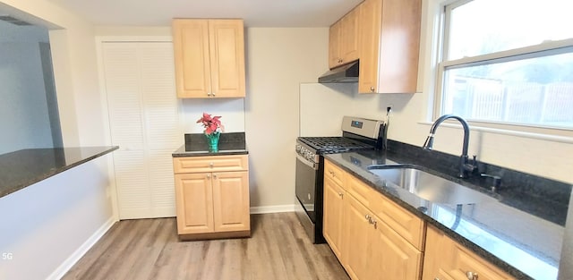 kitchen featuring sink, light brown cabinets, stainless steel gas range, light hardwood / wood-style flooring, and dark stone counters