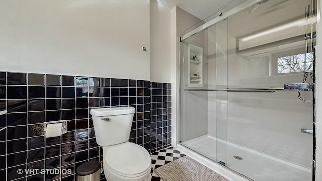 bathroom featuring toilet, a shower with shower door, and tile walls