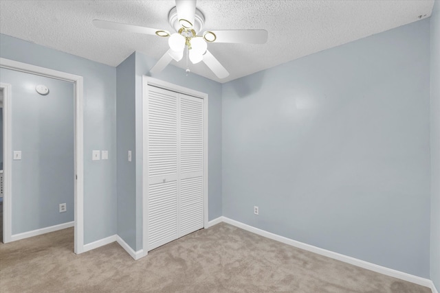 unfurnished bedroom featuring ceiling fan, a closet, light colored carpet, and a textured ceiling