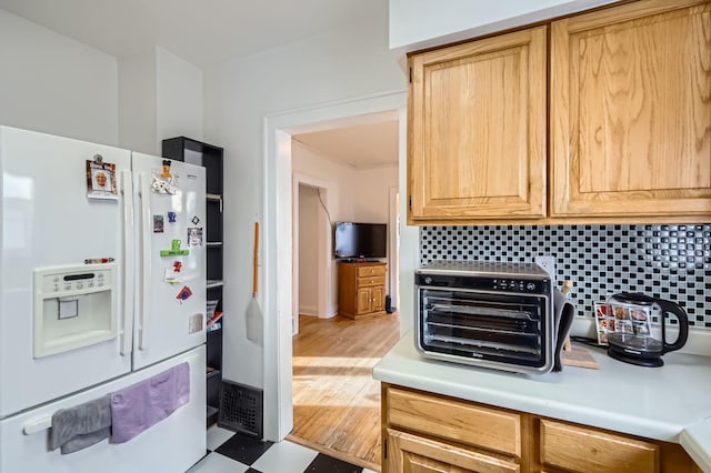 kitchen with white fridge with ice dispenser, light brown cabinetry, and tasteful backsplash