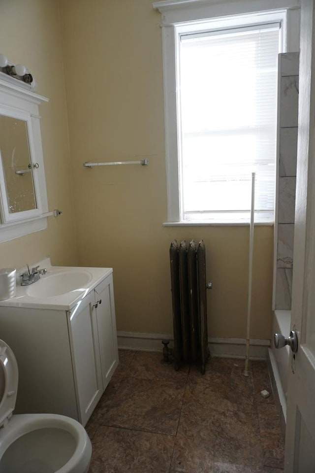 bathroom with radiator heating unit, vanity, toilet, and a wealth of natural light