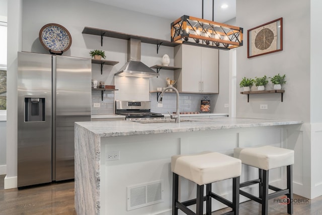 kitchen with appliances with stainless steel finishes, tasteful backsplash, wall chimney range hood, white cabinetry, and a breakfast bar area