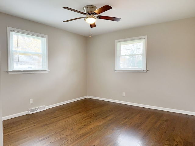 empty room with plenty of natural light, dark wood-type flooring, and ceiling fan